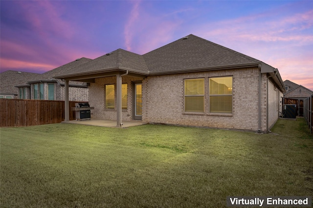 back of property featuring brick siding, roof with shingles, a lawn, and a patio