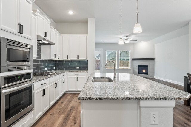 kitchen with a kitchen island with sink, sink, decorative light fixtures, and white cabinets