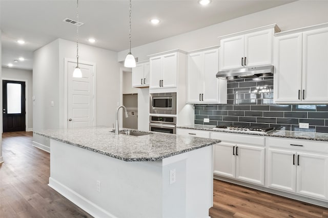 kitchen with appliances with stainless steel finishes, a kitchen island with sink, under cabinet range hood, pendant lighting, and a sink