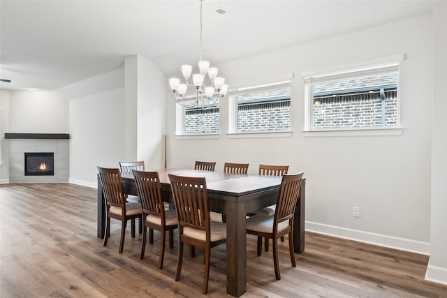 dining area with a tiled fireplace, wood-type flooring, a chandelier, and a healthy amount of sunlight