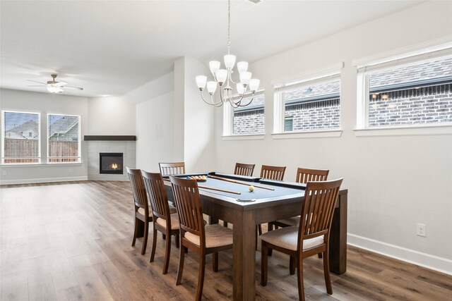 dining area with a tiled fireplace, hardwood / wood-style flooring, and ceiling fan with notable chandelier