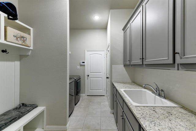 kitchen with gray cabinets, light tile patterned flooring, a sink, washer and dryer, and baseboards