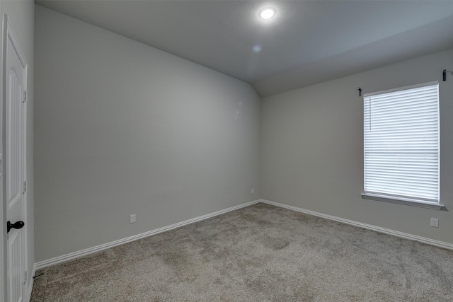 carpeted empty room with vaulted ceiling and baseboards