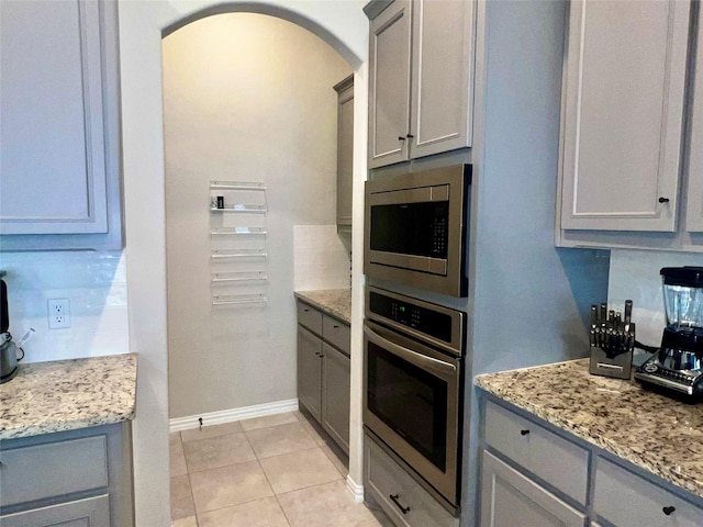 kitchen with light stone counters, appliances with stainless steel finishes, gray cabinets, and light tile patterned floors