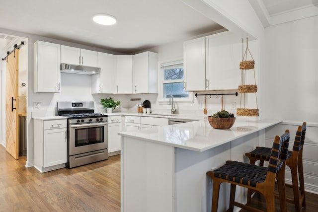 kitchen with stainless steel range with gas cooktop, a barn door, kitchen peninsula, and white cabinets