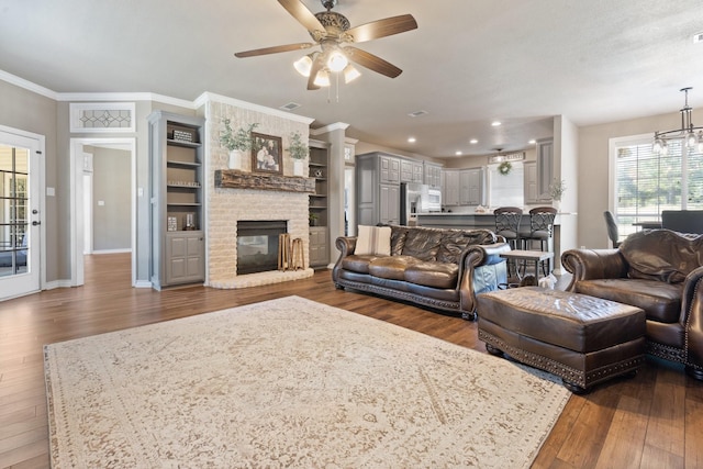 living room with crown molding, a brick fireplace, ceiling fan with notable chandelier, and dark hardwood / wood-style flooring