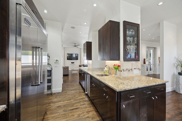 kitchen featuring sink, dark hardwood / wood-style flooring, built in fridge, light stone countertops, and backsplash