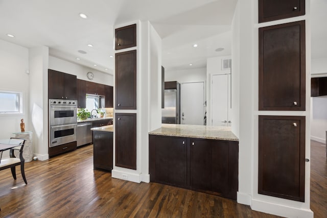 kitchen with light stone counters, appliances with stainless steel finishes, dark hardwood / wood-style flooring, and dark brown cabinets