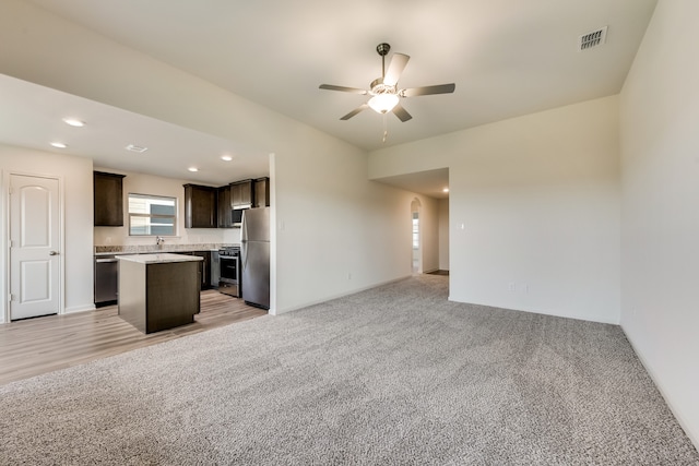 kitchen featuring a center island, dark brown cabinets, light carpet, appliances with stainless steel finishes, and ceiling fan