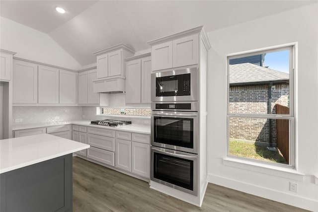 kitchen with light countertops, appliances with stainless steel finishes, wood finished floors, vaulted ceiling, and backsplash