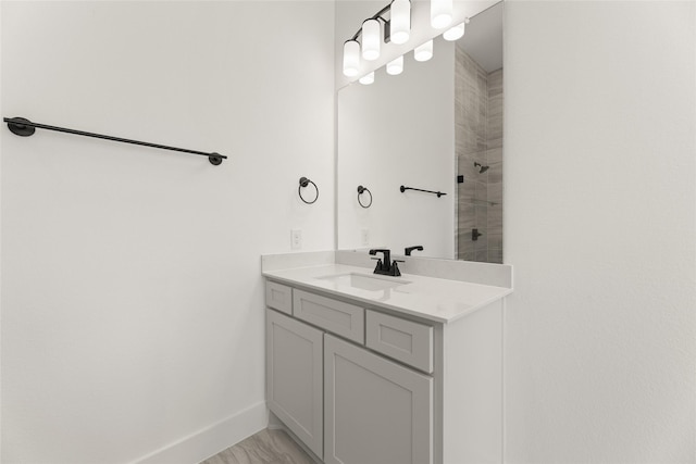 full bathroom with a tile shower, vanity, and baseboards