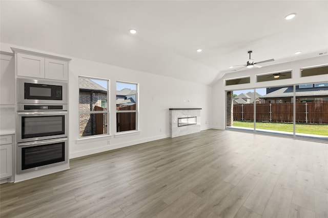 unfurnished living room with light wood-style flooring, a ceiling fan, a premium fireplace, and a healthy amount of sunlight