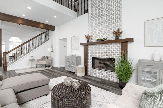 living area featuring stairs, a towering ceiling, wood finished floors, recessed lighting, and a tiled fireplace