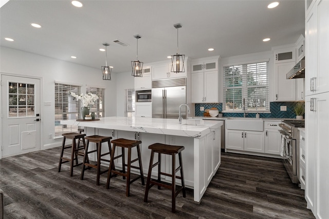 kitchen featuring a spacious island, sink, white cabinetry, built in appliances, and range hood