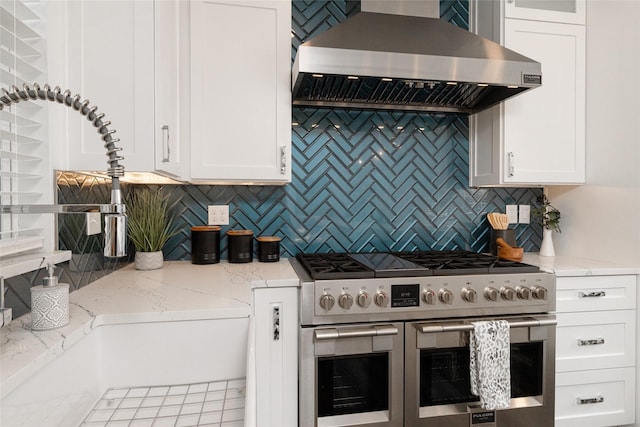 kitchen featuring white cabinets, backsplash, range with two ovens, light stone counters, and wall chimney range hood