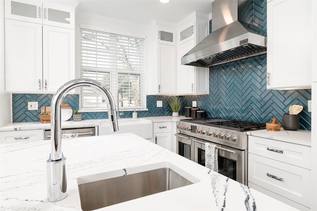 kitchen featuring wall chimney exhaust hood, range with two ovens, decorative backsplash, and white cabinetry