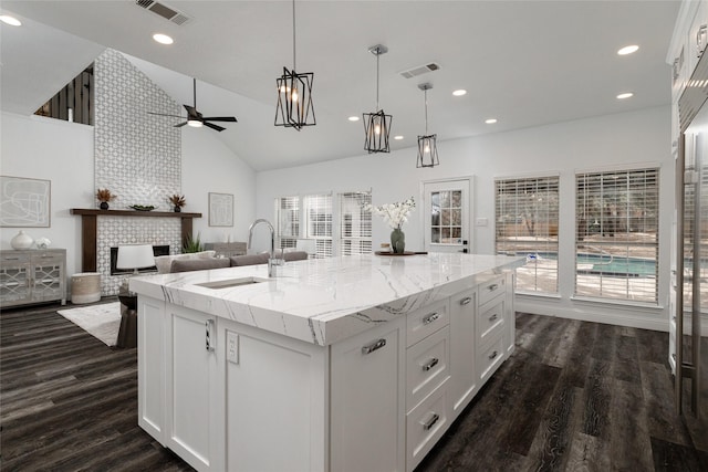 kitchen with pendant lighting, white cabinetry, sink, light stone counters, and a center island with sink