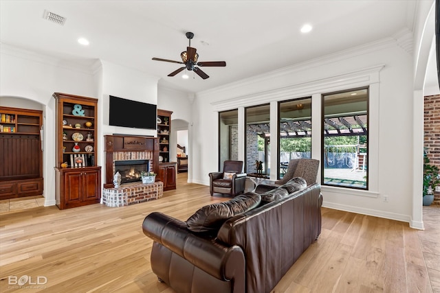 living room featuring ceiling fan, ornamental molding, a fireplace, and light wood-type flooring