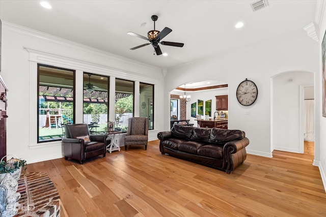 living room with ceiling fan with notable chandelier, ornamental molding, sink, and light hardwood / wood-style floors