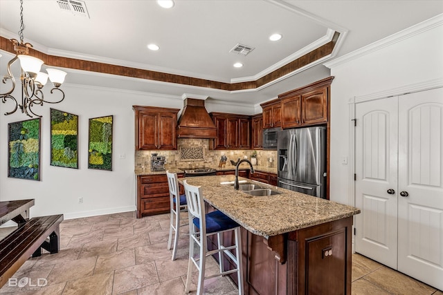 kitchen featuring sink, custom exhaust hood, stainless steel refrigerator with ice dispenser, light stone countertops, and a center island with sink