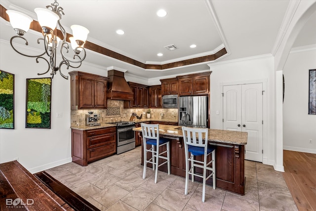 kitchen with decorative light fixtures, custom exhaust hood, light stone counters, stainless steel appliances, and a center island with sink