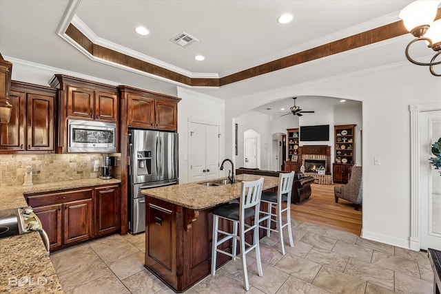 kitchen featuring sink, a breakfast bar area, a kitchen island with sink, stainless steel appliances, and light stone countertops