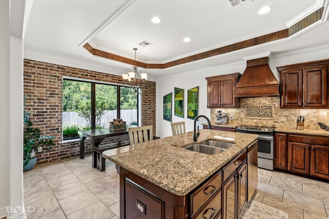 kitchen featuring sink, custom exhaust hood, a kitchen island with sink, a tray ceiling, and stainless steel appliances