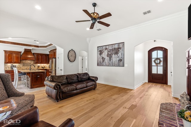 living room with crown molding, ceiling fan, sink, and light hardwood / wood-style floors