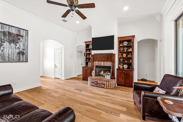 living room with crown molding, ceiling fan, a brick fireplace, and light hardwood / wood-style flooring