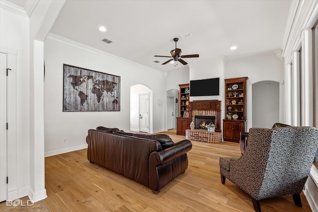 living room featuring ceiling fan, ornamental molding, light hardwood / wood-style floors, and a brick fireplace