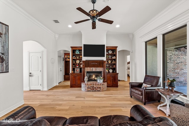 living room featuring ornamental molding, ceiling fan, a fireplace, and light hardwood / wood-style flooring