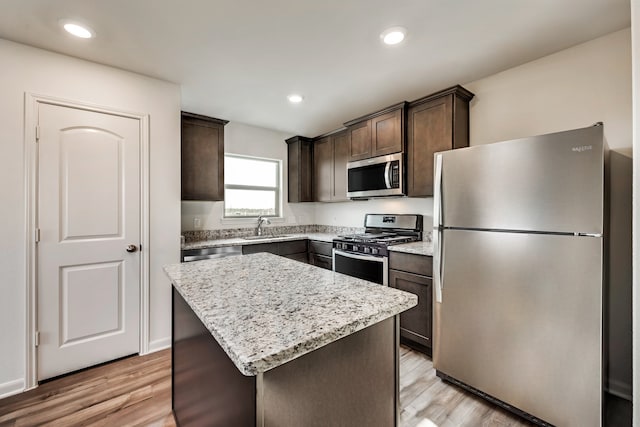 kitchen with appliances with stainless steel finishes, a center island, sink, and light wood-type flooring