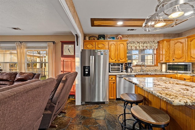 kitchen with sink, appliances with stainless steel finishes, hanging light fixtures, a kitchen breakfast bar, and light stone counters