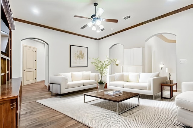 living area with light wood-style floors, arched walkways, visible vents, and crown molding