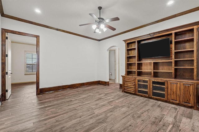 unfurnished living room featuring baseboards, arched walkways, ceiling fan, ornamental molding, and wood finished floors