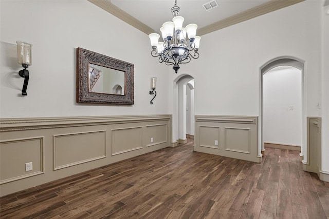 unfurnished dining area featuring visible vents, arched walkways, dark wood-style floors, crown molding, and a decorative wall