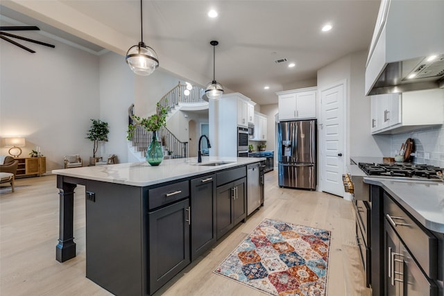 kitchen featuring white cabinetry, hanging light fixtures, a center island with sink, custom range hood, and stainless steel appliances