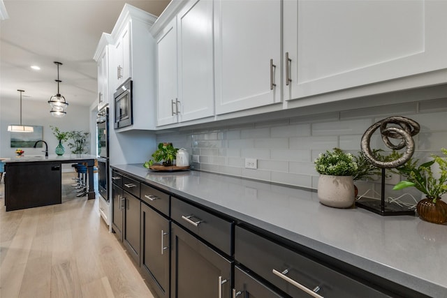 kitchen featuring light hardwood / wood-style flooring, hanging light fixtures, stainless steel appliances, decorative backsplash, and white cabinets