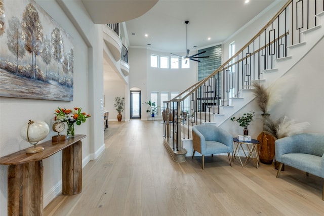 foyer entrance with crown molding, a towering ceiling, ceiling fan, and light hardwood / wood-style flooring