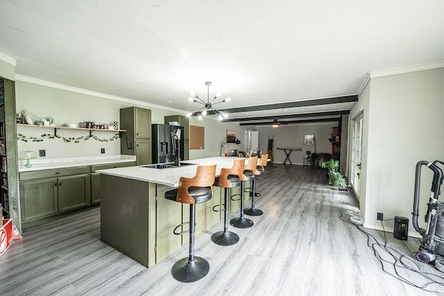 kitchen featuring a kitchen bar, a kitchen island with sink, a notable chandelier, black fridge, and light hardwood / wood-style flooring