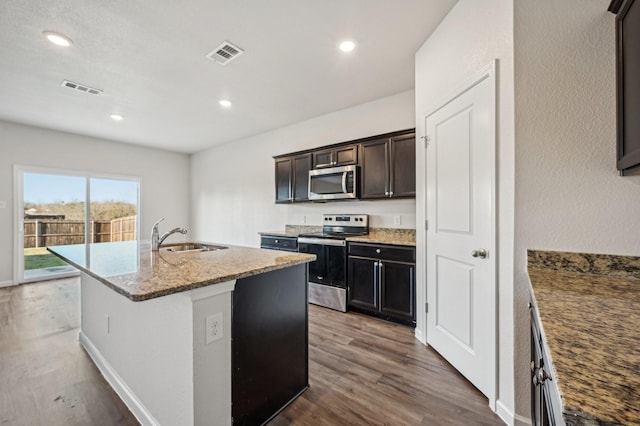 kitchen featuring appliances with stainless steel finishes, an island with sink, sink, hardwood / wood-style flooring, and light stone counters