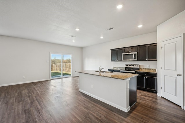 kitchen featuring sink, appliances with stainless steel finishes, a kitchen island with sink, dark hardwood / wood-style floors, and light stone counters