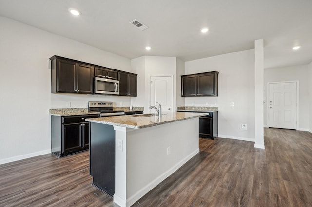 kitchen featuring sink, light stone counters, a center island with sink, dark hardwood / wood-style floors, and stainless steel appliances