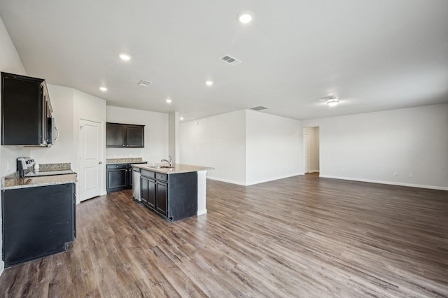 kitchen with sink, light stone counters, a center island with sink, dark hardwood / wood-style flooring, and stove