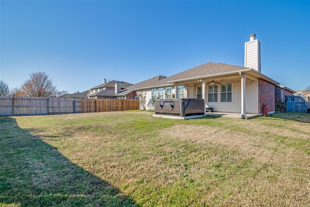 rear view of house with a hot tub, a patio, and a yard