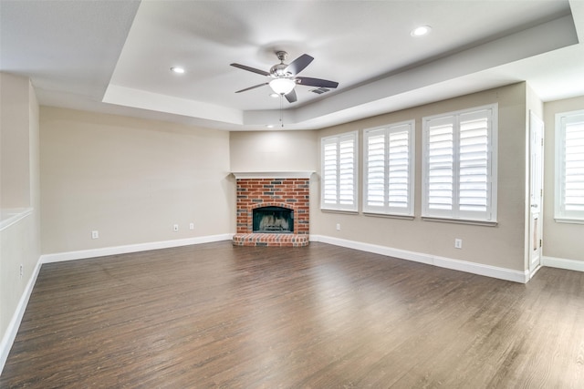 unfurnished living room featuring a raised ceiling, plenty of natural light, dark wood-type flooring, and a fireplace