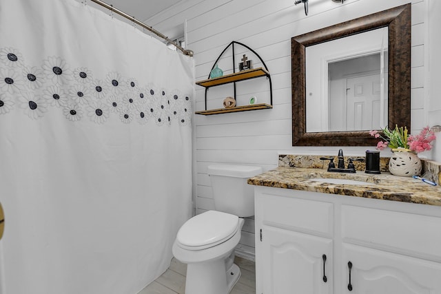 bathroom featuring vanity, a shower with shower curtain, wooden walls, and toilet