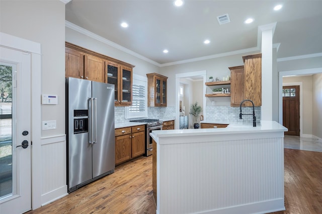 kitchen with stainless steel appliances, kitchen peninsula, a healthy amount of sunlight, and light wood-type flooring