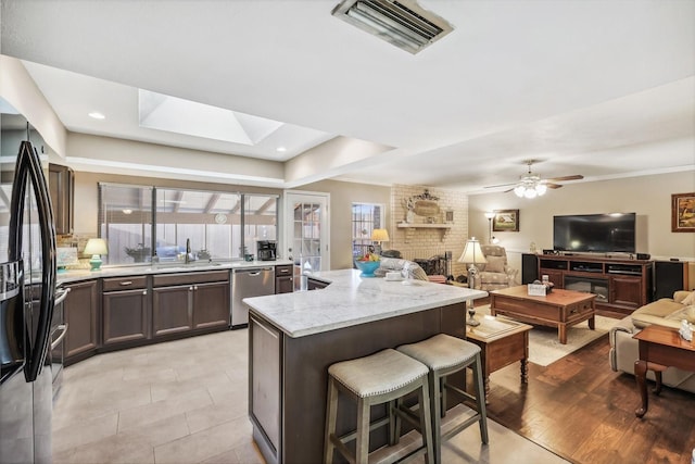 kitchen with black fridge with ice dispenser, sink, light stone counters, stainless steel dishwasher, and a wealth of natural light