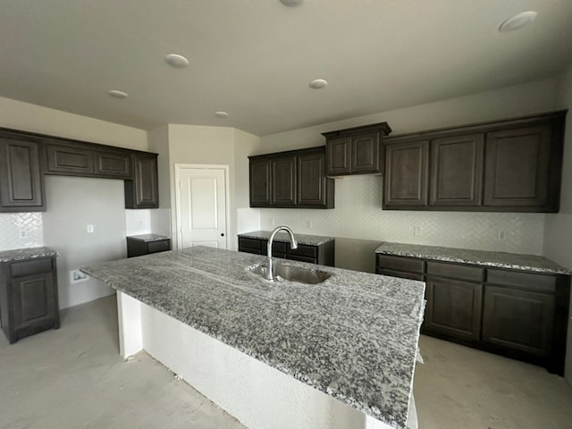 kitchen featuring light stone countertops, sink, a center island with sink, and decorative backsplash